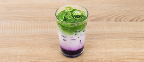 Iced Blackberry matcha latte in glass on a wooden surface