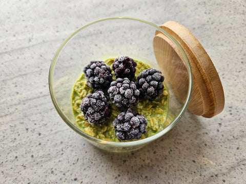 matcha overnight oats topped with frozen blackberries in a glass jar